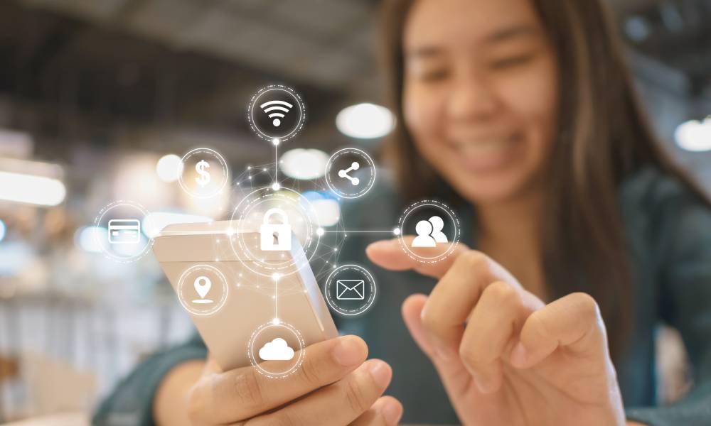 A woman smiling as she holds her phone. Above the phone is a network of symbols representing security and connectivity.