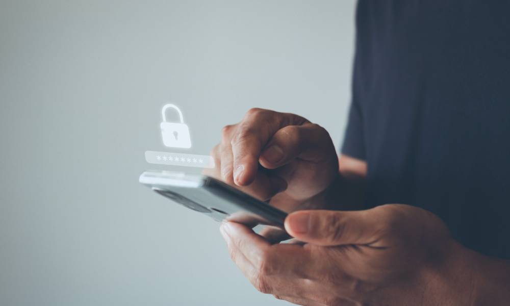 A man holding a smart phone. Above the phone is a graphic of a white padlock and a hidden password bar.