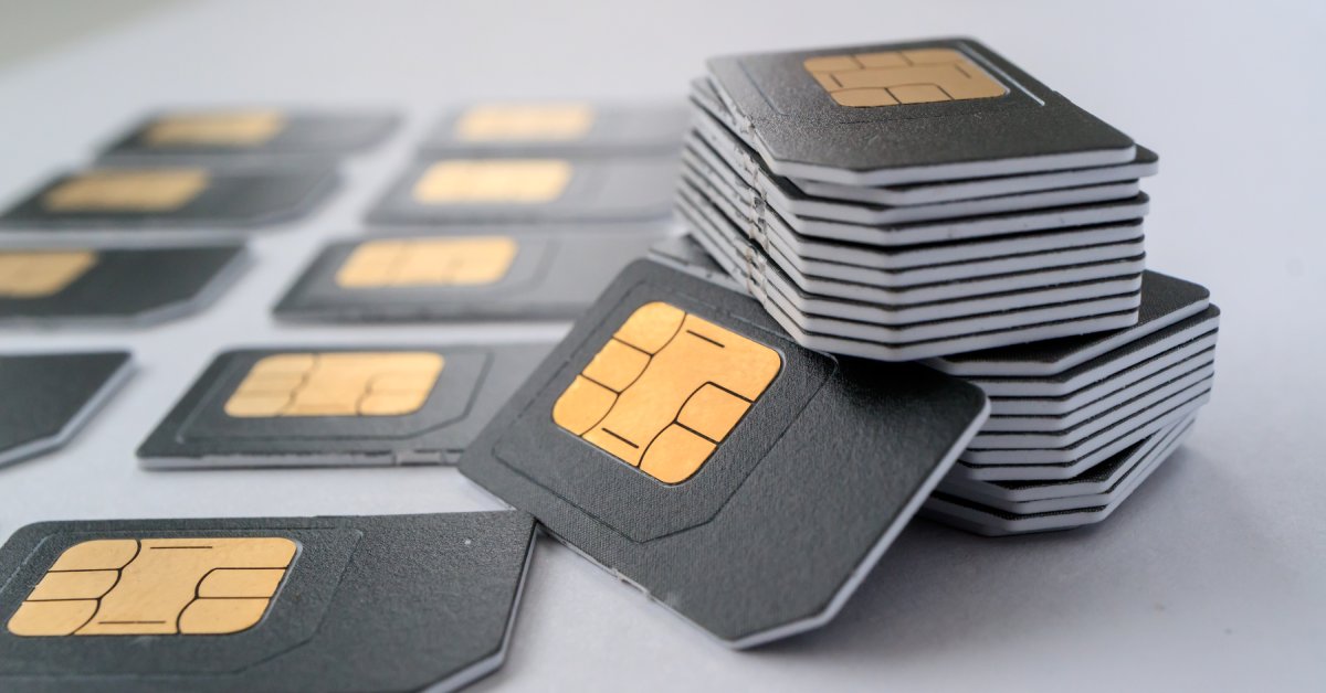 A large stack of black SIM cards is sitting on a gray table. Some SIM cards are lined up on the table next to the stack.