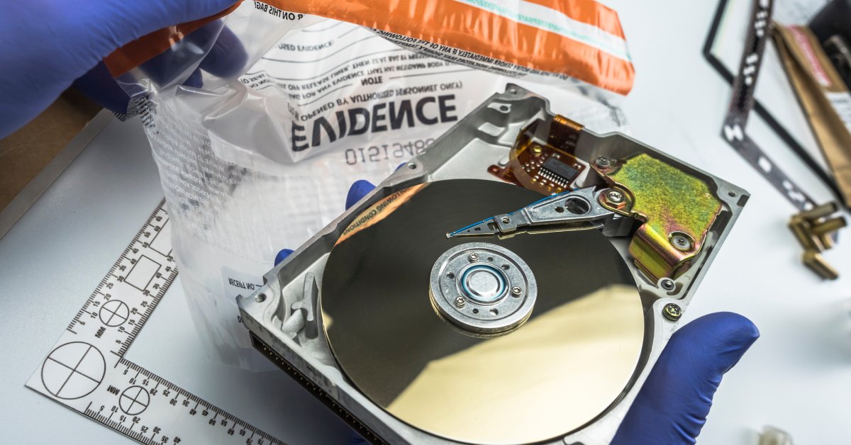 A person wearing blue gloves is holding a hard drive. They are placing the hard drive in a bag that reads “Evidence.”