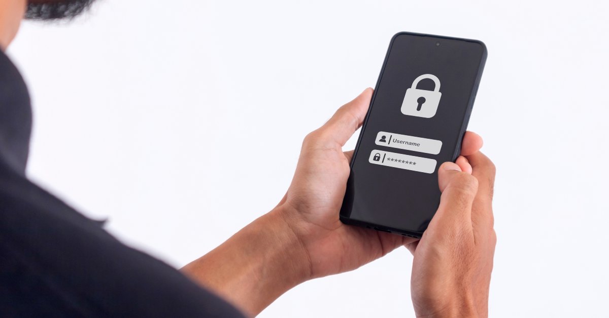 A man holds a cell phone in both hands. There is a lock, username, and password on the phone screen.