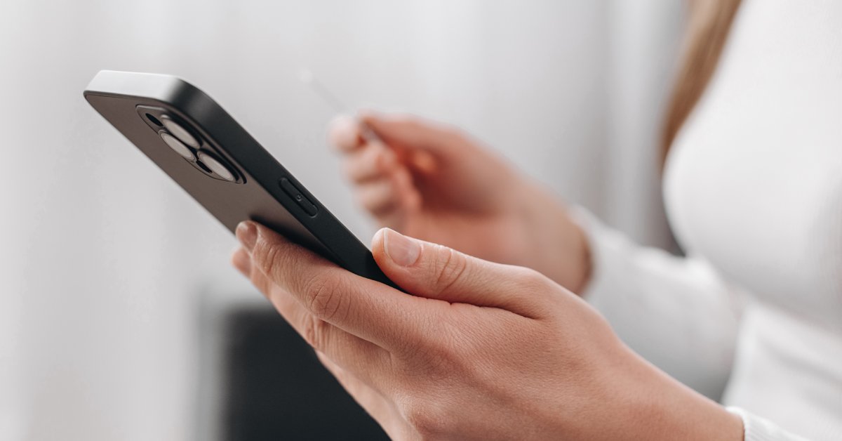 A close-up of a person holding a black smartphone in one hand and a credit card in the opposite hand.