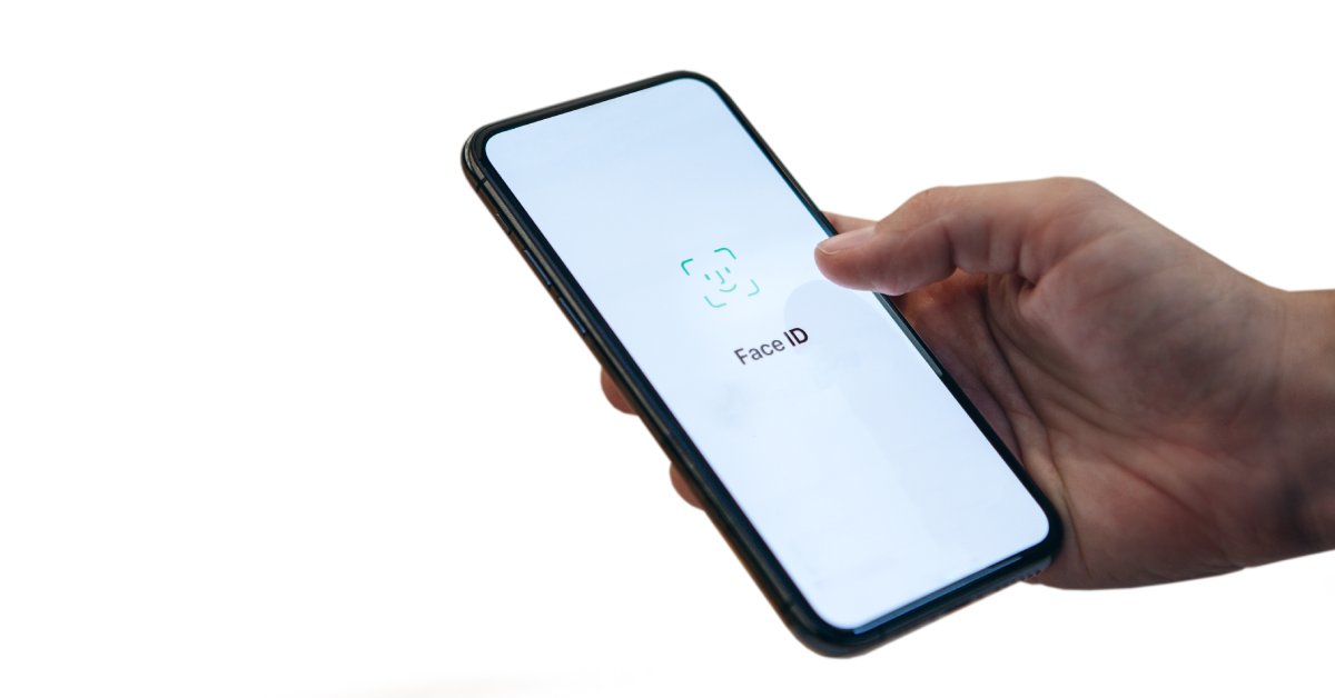 A close-up of someone holding a cell phone in their hand. The screen is white with "Face ID" on the screen.