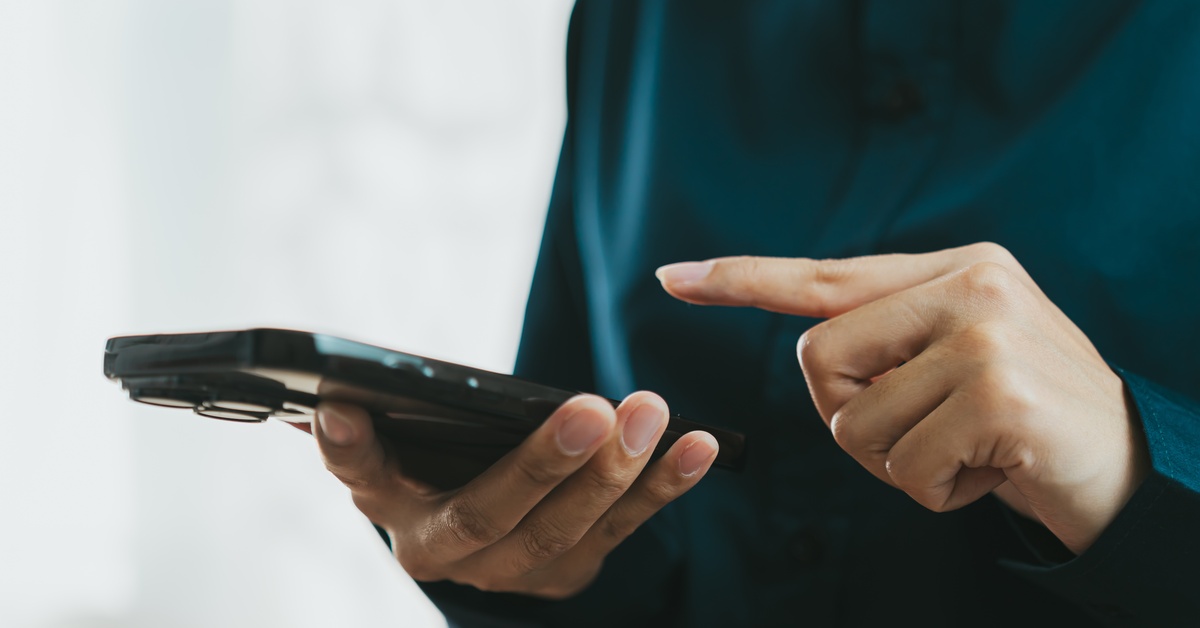 A close-up of a person holding a black smartphone and using their pointer finger to touch the screen.