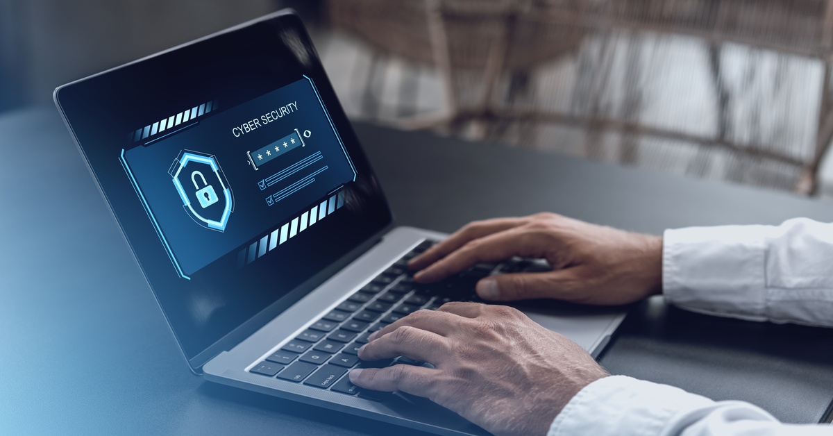 Someone's hands rest on the keyboard of a laptop. The screen shows a lock with "CYBER SECUIRTY" at the top.